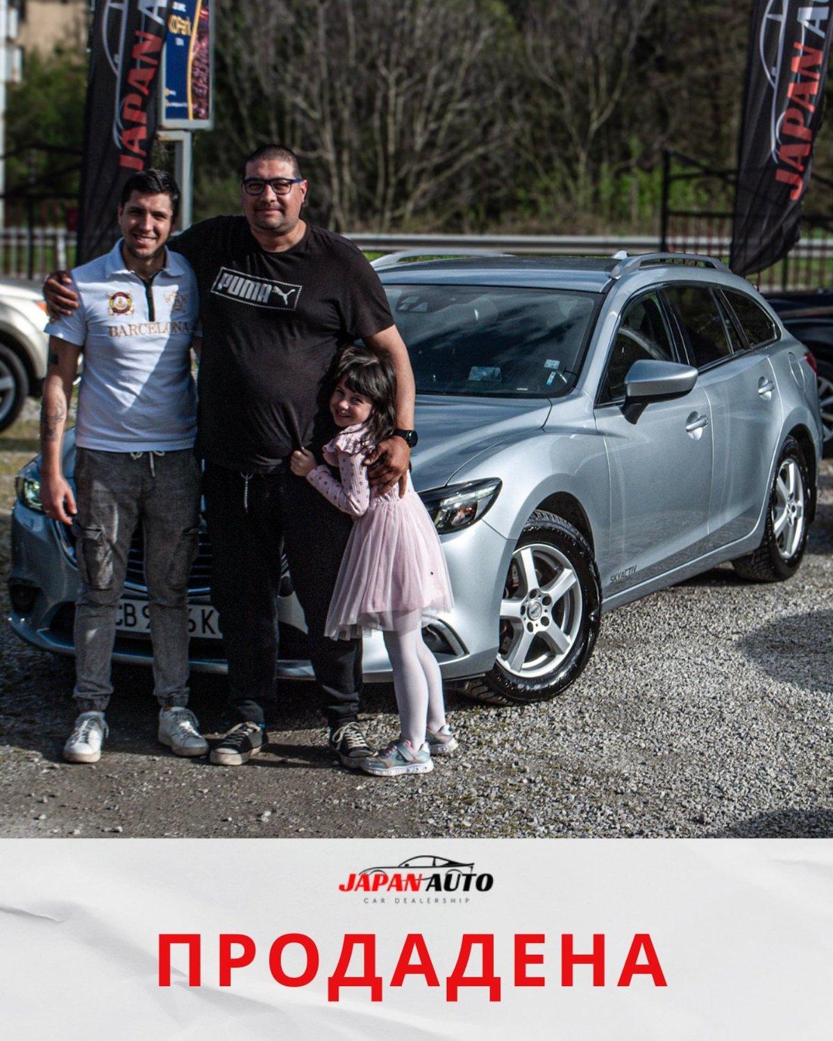 Two men and a young girl stand beside a silver car at an auto dealership