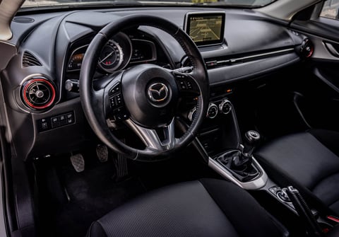 Mazda sports car interior featuring black leather steering wheel, dashboard, manual transmission shifter, and red circular air vents
