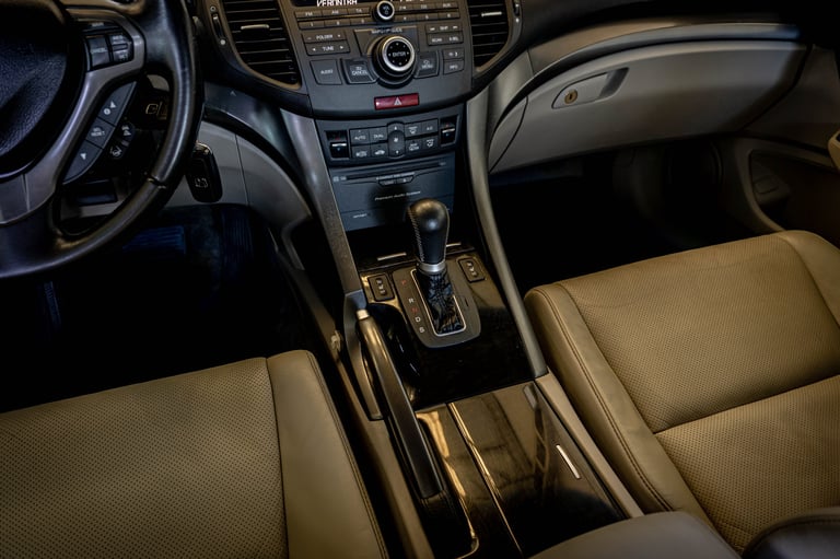 Luxury car interior with tan leather seats, dark steering wheel, center console controls, and automatic transmission shifter