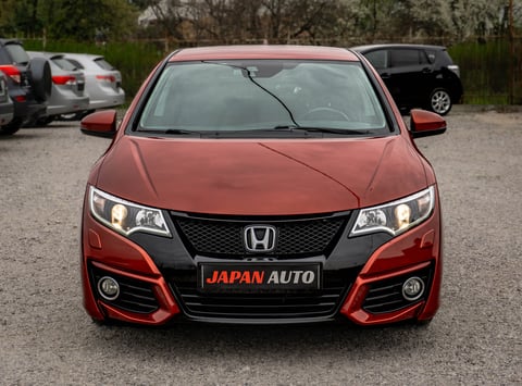 Red Honda sedan with JAPAN AUTO license plate displayed at a car dealership lot with other vehicles parked in background