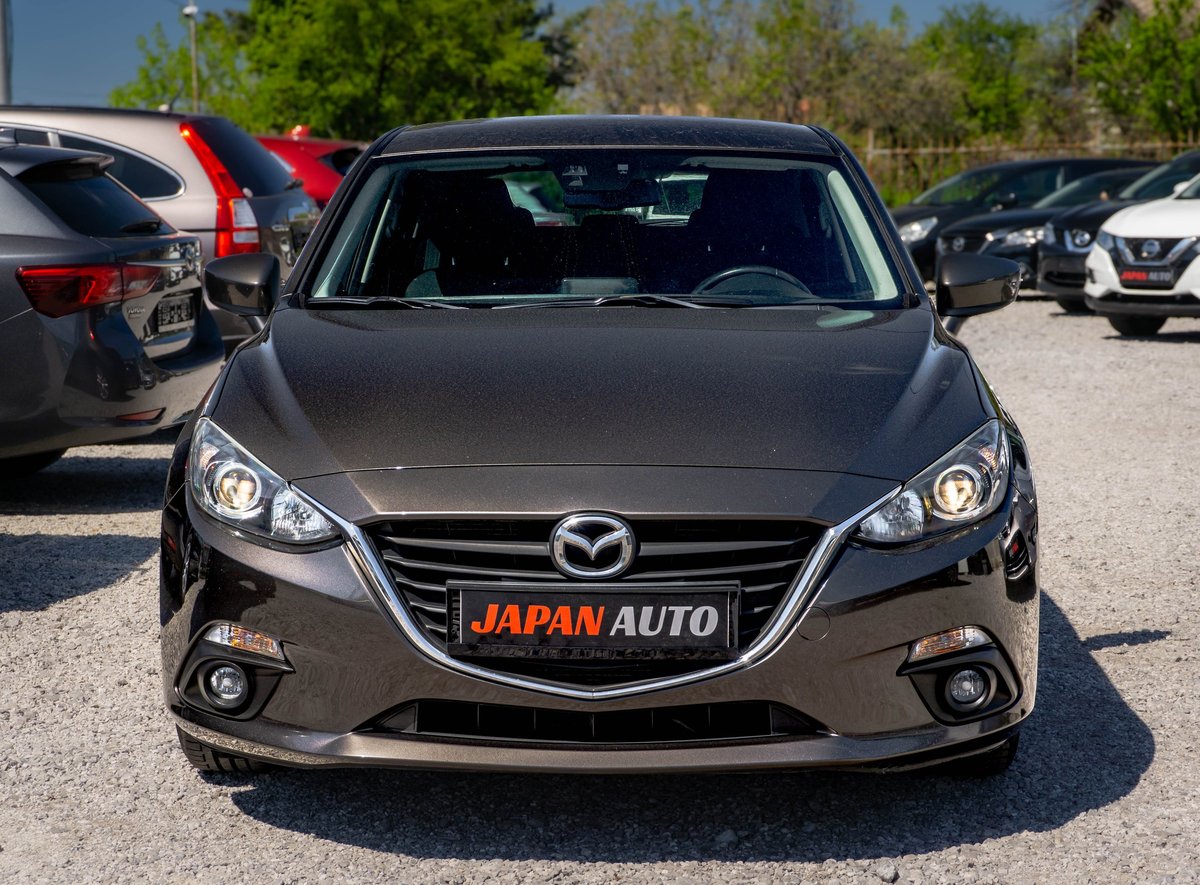 Front view of a gray Mazda sedan with Japan Auto dealership plate in outdoor parking lot