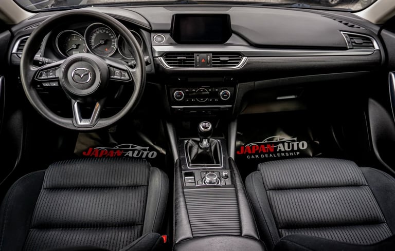 Interior view of a Mazda vehicle dashboard and steering wheel with black ribbed seats and center console