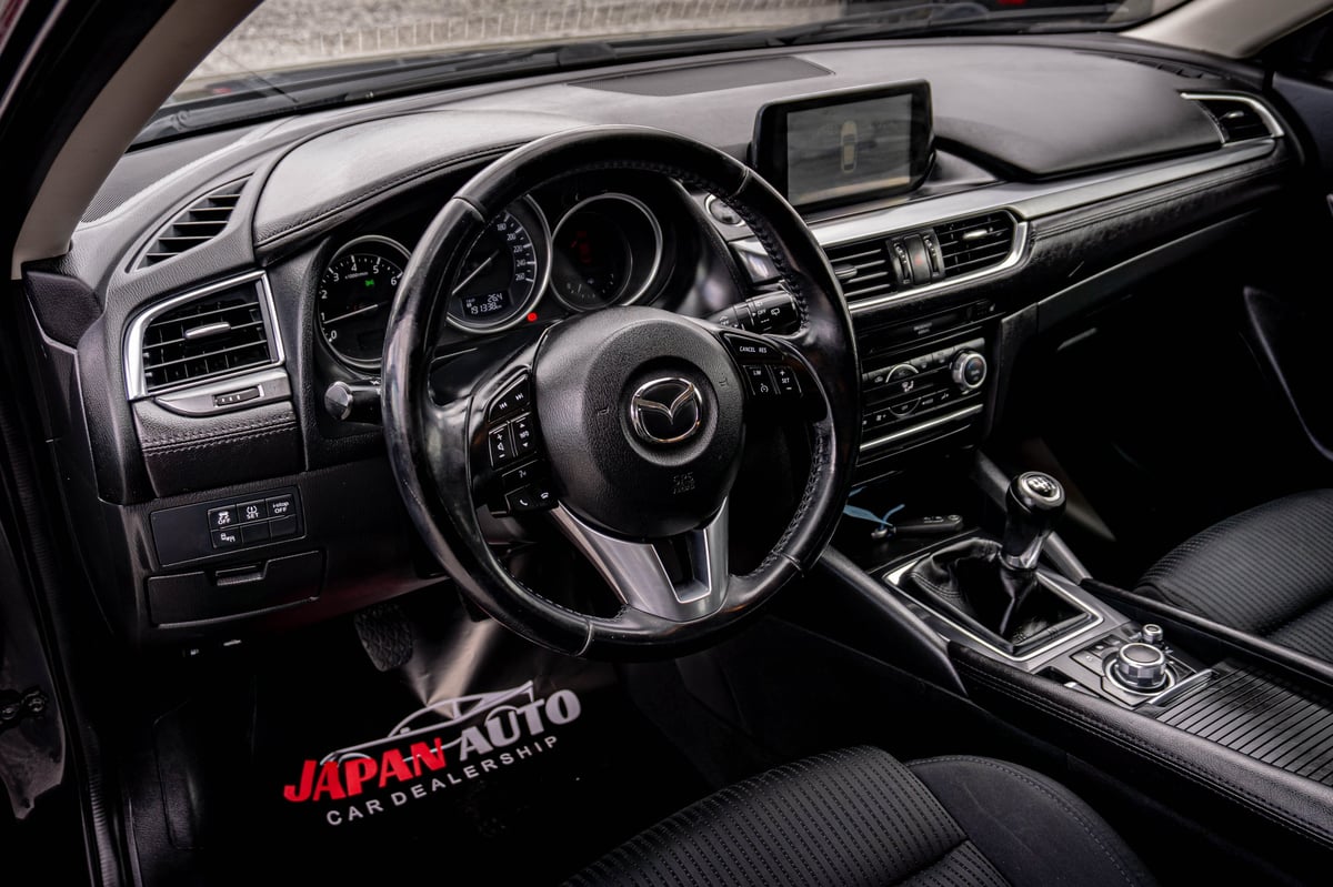 Modern Mazda car interior showing steering wheel, dashboard, touchscreen display, and manual transmission with Japan Auto logo