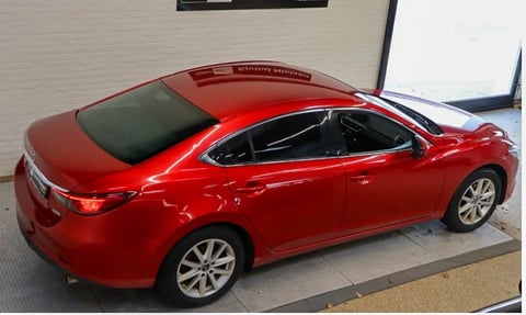 Red four-door sedan parked on pavement outside a building