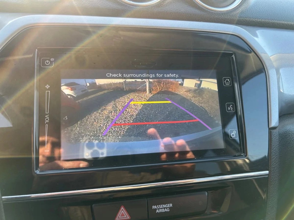 Car backup camera display showing rear view with colored distance guide lines and check surroundings safety message