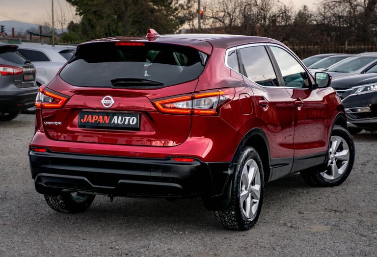 Red Nissan SUV parked in a lot with Japan Auto dealership sign visible on the rear bumper