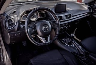 Interior of a Mazda vehicle showing steering wheel, dashboard with display screen, and black upholstered seats