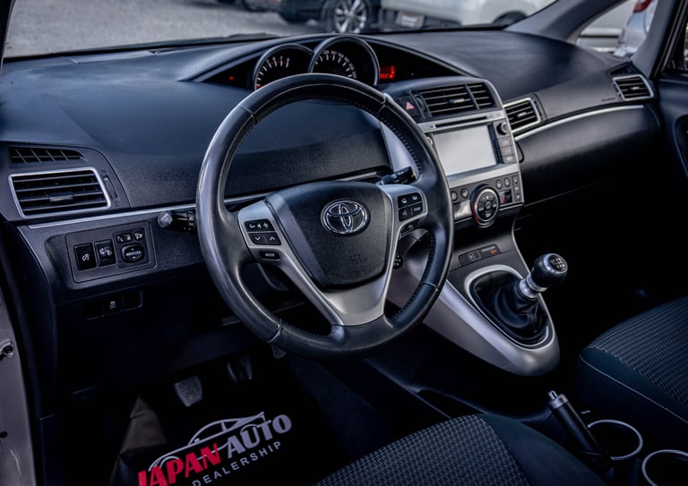 Interior view of a Toyota vehicle showing the steering wheel, dashboard, and control panel with another car visible in the background