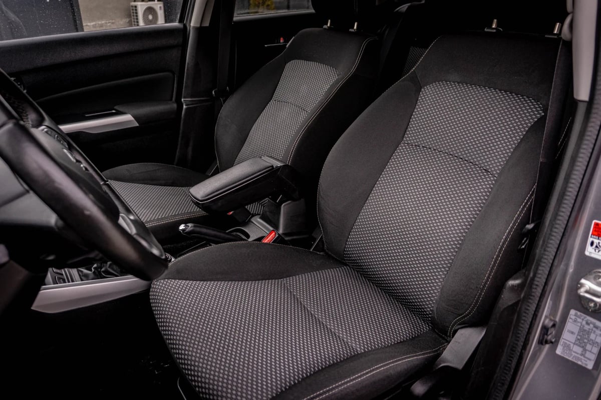 Car interior showing black fabric seat covers on front seats with gray stitching pattern and steering wheel visible