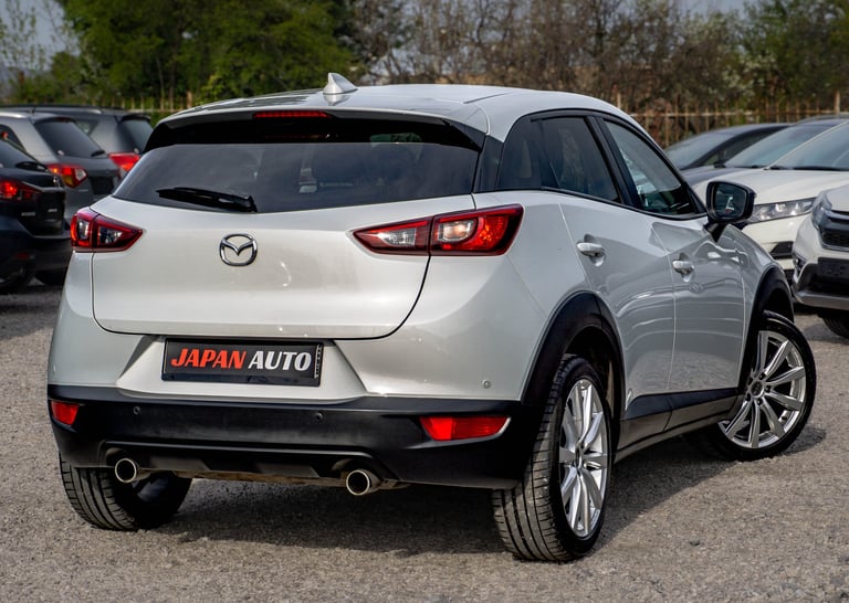White Mazda CX-3 SUV parked in a lot, rear view showing dual exhaust, red taillights, and JAPAN AUTO license plate