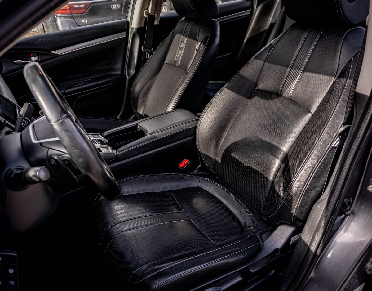 Car interior showing black leather front seats with gray striping, steering wheel, and dashboard visible through open driver-side door