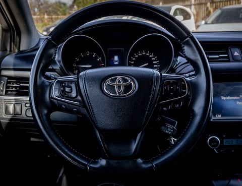 Toyota steering wheel with logo, instrument cluster visible in background inside vehicle interior