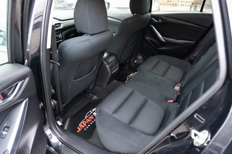 Interior view of vehicle rear seats showing black leather upholstery with open door and windows visible