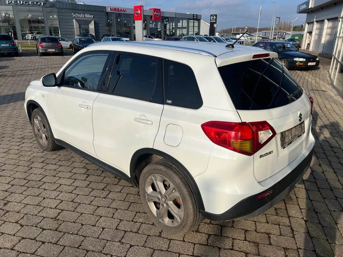 White compact SUV parked on brick pavement at a car dealership with showroom buildings in background