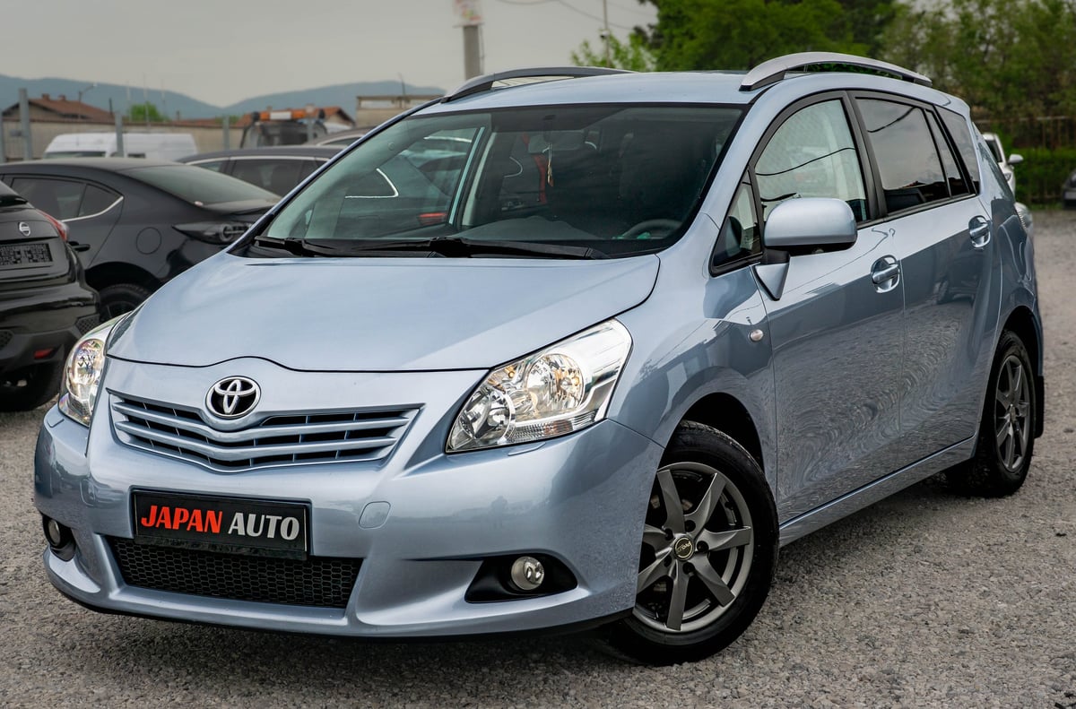 Silver Toyota minivan parked at a dealership lot with mountains in background