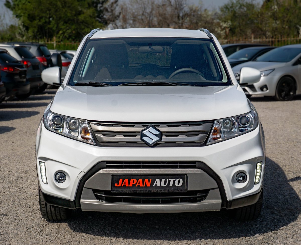 White Suzuki SUV with Japan Auto license plate displayed at car dealership lot with other vehicles in background