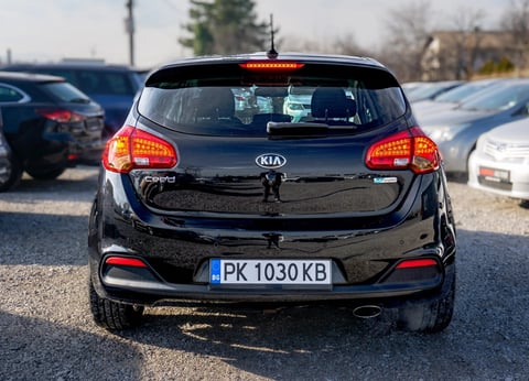 Black Kia hatchback car photographed from behind in a parking lot, showing rear lights and license plate