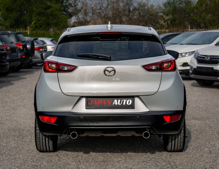 Rear view of white Mazda CX-3 compact SUV in parking lot with other vehicles