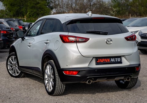 White Mazda compact SUV photographed from rear angle in a dealer lot with other vehicles visible