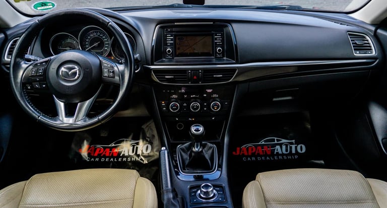 Mazda car interior dashboard with steering wheel, infotainment system, and beige leather seats viewed from front