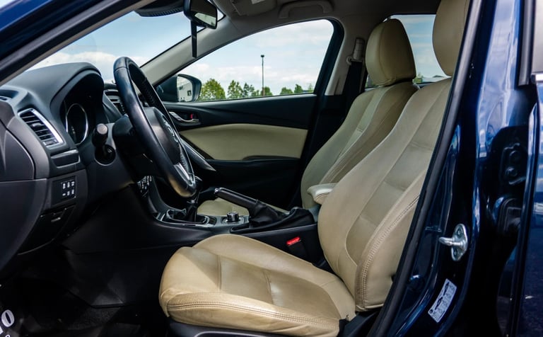 Interior of blue sports car showing tan leather seats, steering wheel, dashboard, and view through windshield of outdoor scenery