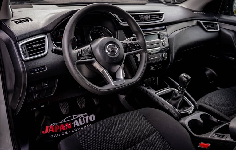 Modern car interior featuring a black steering wheel, dashboard, and center console with a gear shift, displayed at Japan Auto car dealership