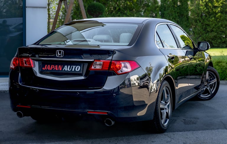 Black Honda sedan parked on driveway with Japan Auto dealership plate, green foliage in background
