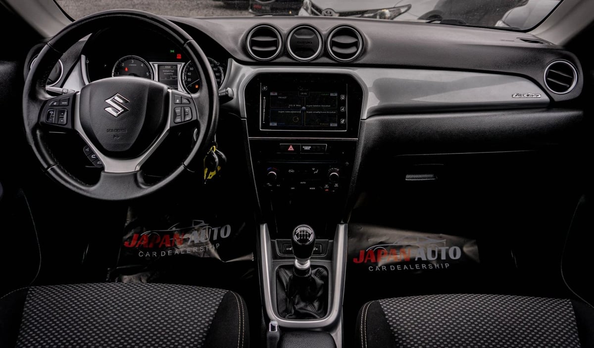 Interior view of Suzuki car dashboard with steering wheel, center console, and black upholstered seats