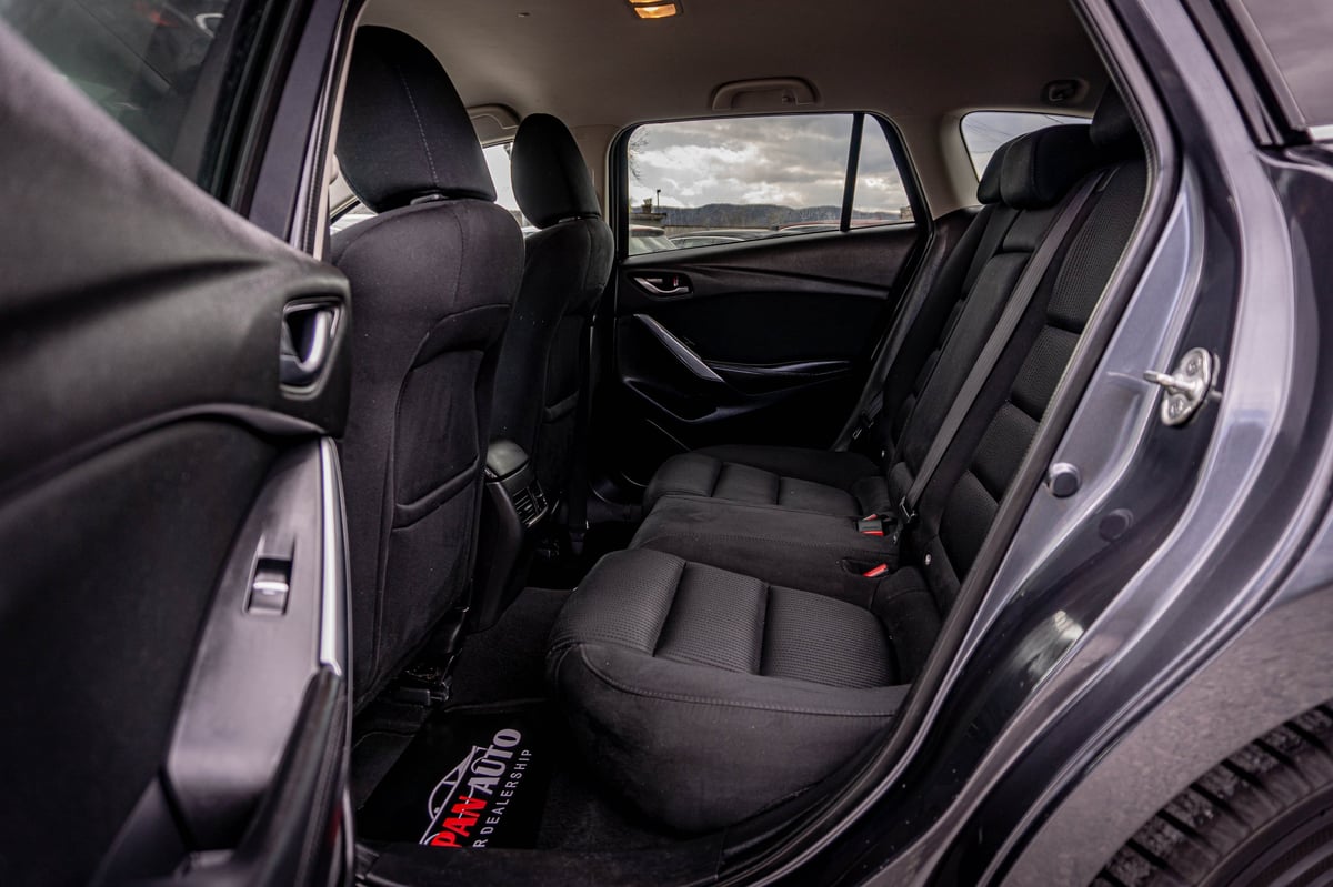 Interior view of a cars rear seating area with black upholstered seats and open door showing side windows and landscape view