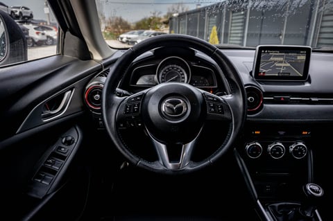 Mazda vehicle interior showing steering wheel, dashboard with infotainment screen, and climate controls