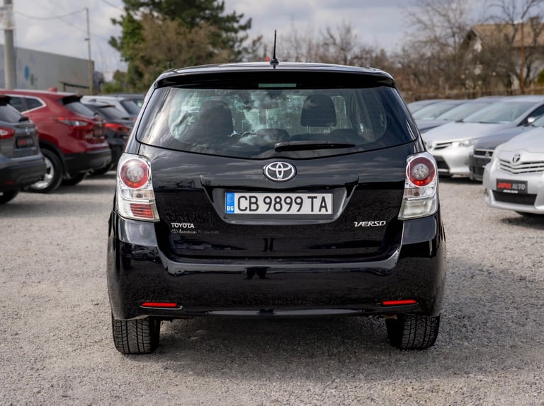 Rear view of a black Toyota Verso minivan in a car dealership lot with other vehicles visible in the background