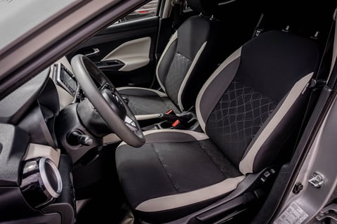 Car interior showing black and beige leather seats, steering wheel, and dashboard from side angle