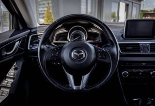 Interior view of a Mazda vehicle showing the steering wheel, dashboard, and touchscreen display with bright natural lighting from windows