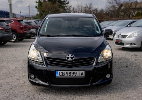 Front view of a black Toyota Avensis sedan in a parking lot with other vehicles in the background