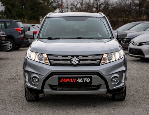Silver Suzuki SUV with JAPAN AUTO badging parked at a dealership lot with other vehicles in background