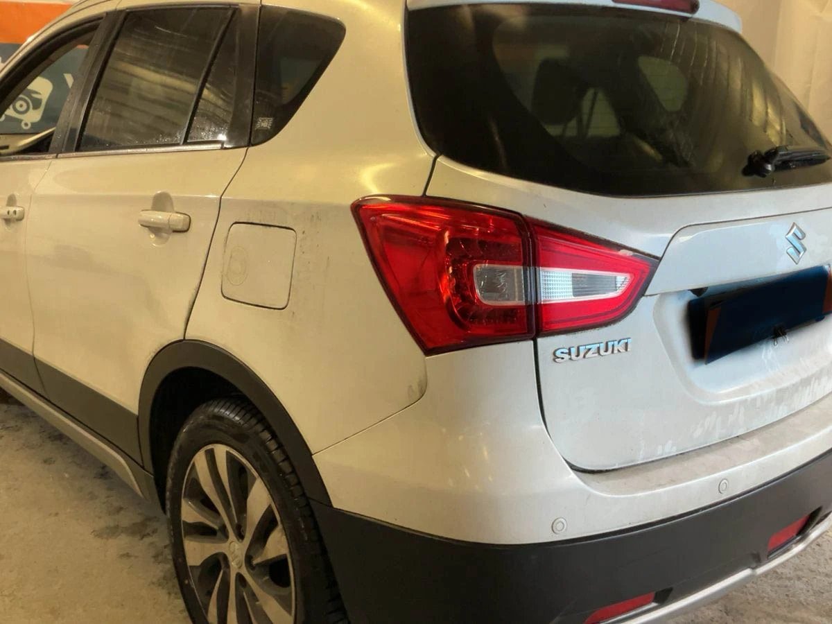 Rear view of white Suzuki vehicle parked indoors, showing taillights and alloy wheel